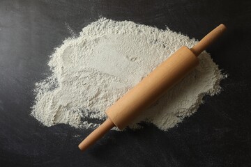 Flour and rolling pin on black table, top view