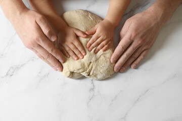 Father and child making dough at white table, top view