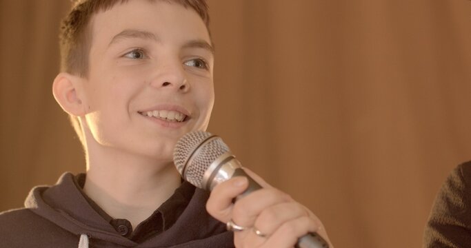 Close-up teenage student speaks into microphone during school debate. 7th grader confidently expresses opinion. Talking boy showcasing budding eloquence and critical thinking skills on stage in school