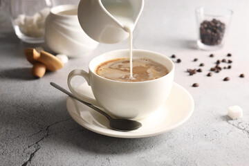 Pouring milk into cup with coffee on light grey textured table, closeup