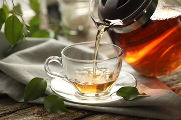 Pouring tea into cup on wooden table, closeup