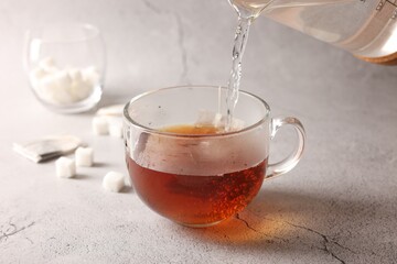 Pouring hot water into cup with tea bag on light grey textured table, closeup