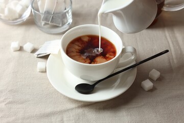 Pouring milk into cup with tea on light table, closeup
