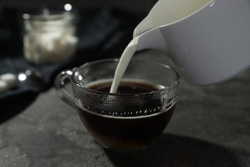 Pouring milk into cup of coffee on grey table, closeup