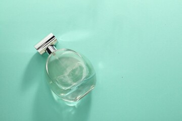 Luxury perfume in bottle on turquoise background, top view. Space for text