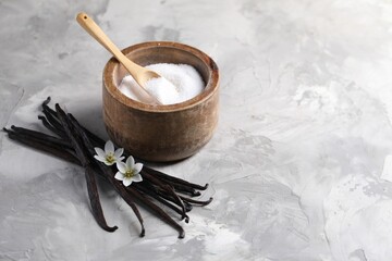 Vanilla pods, flowers and bowl with sugar on light textured table, closeup. Space for text