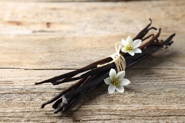 Bunch of vanilla pods and flowers on wooden table, closeup. Space for text