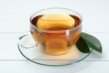Aromatic tea in glass cup and green leaves on white wooden table