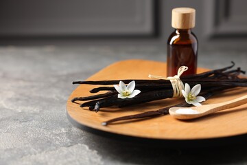 Bunch of vanilla pods, flowers, sugar and bottle with essential oil on grey textured table,...