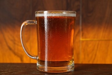 Mug with fresh beer on wooden table against color background, closeup