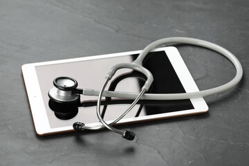 Modern tablet and stethoscope on black table
