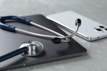 Modern electronic devices and stethoscope on grey table, closeup