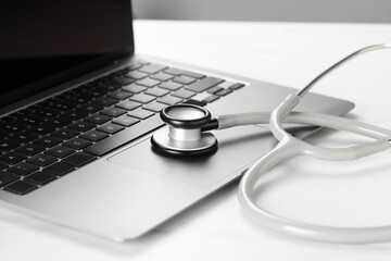 Modern laptop and stethoscope on white table, closeup