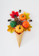 Ice cream cone with autumn leaves, pumpkins, acorns and pinecones on white background. Minimal...