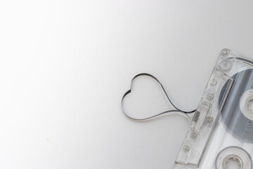 An old vintage cassette tape with the tape being pulled out in the shape of a heart on a white...