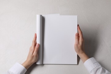 Woman holding notebook with blank pages at white table, top view. Mockup for design