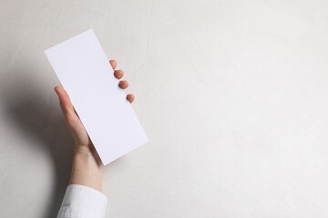 Woman holding blank card at white table, top view. Mockup for design