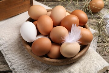 Fresh chicken eggs in bowl and dried hay on wooden table
