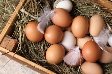 Fresh chicken eggs and dried hay in wooden crate on table, top view