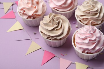Delicious birthday cupcakes, sprinkles and bunting flags on violet background, closeup