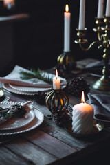 Beautiful table setting for family Christmas dinner at home. Cozy atmosphere, candlelight. Wine glasses, vintage chandelier, elegant interior. Fir tree branches, wooden furniture, dark, bokeh