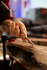 Manufacturer meticulously carving intricate designs into wood using chisel and hammer in carpentry...
