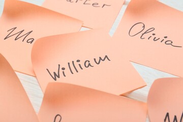 Paper stickers with different names on white wooden table, closeup. Choosing baby's name