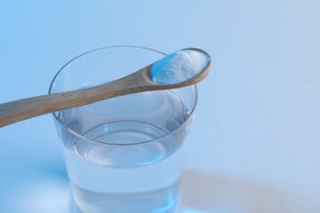 Glass of water and spoon with baking soda on light blue background, closeup. Space for text