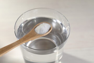 Spoon with baking soda over glass of water on light background, closeup