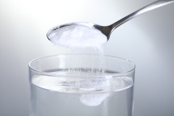 Adding baking soda into glass of water on light grey background, closeup