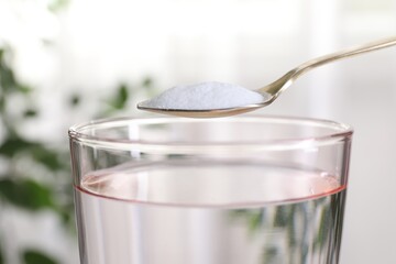 Spoon with baking soda over glass of water on blurred background, closeup