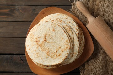 Many tasty homemade tortillas and rolling pin on wooden table, top view