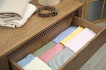 Chest of drawers with different folded clothes and belt indoors