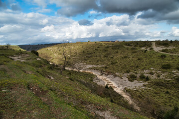 Image of dry creek, dirt and rocks within the creek bed and lined with mature green trees and rocks. In the Basque Country, Spain



