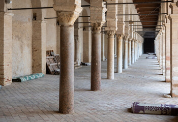 Obraz premium Long corridors under vaulted ceiling in ancient mosque of Kairouan in Tunisia. Colonnade in patio of Islamic temple. Religious Islamic building, place of worship prayer for many generations of Muslims