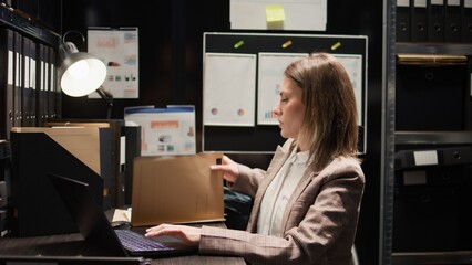 Close-up of caucasian female detective closing laptop and folder, leaving her workstation. After...