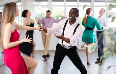 Smiling lady and man training swing dance in pair in dance-hall during dancing classes