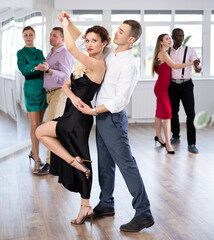 Fototapeta premium With unhurried music, man with woman in couple spins to rhythm of waltz during lesson for novice students. Classes in mini-groups for those who want to learn dancing