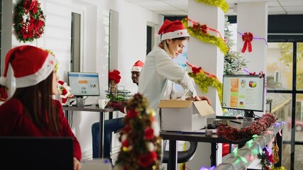 Upset worker in festive decorated office packs desk belongings on last day at work. Employee...
