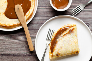 Preparing Argentinian crepes with dulce de leche and icing sugar in white plates on wooden...