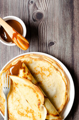 Argentinian crepe filled with dulce de leche and a bowl of dulce de leche on wooden background. 