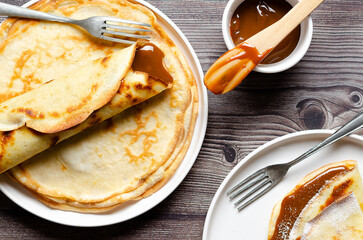 Argentinian crepes filled with dulce de leche in white plates on wooden background. 