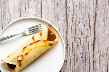 Argentinian crepe filled with dulce de leche in a white plate on wooden background with copy space.  