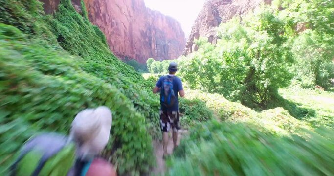 Hikers on narrow dirt path in small  green valley 