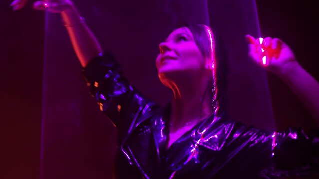 Classy woman in latex coat, violet laser illumination light, neon. Model dancing