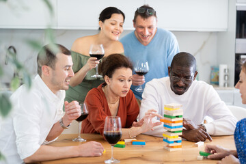 Merry male and female friends engaged in brick game while having red wine in comfort of their house