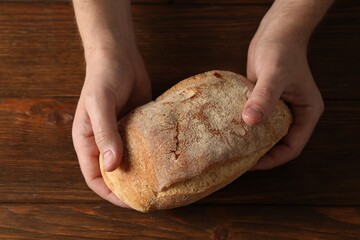 Man holding loaf of fresh bread at wooden table, top view