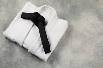 Black karate belt and white kimono on gray textured background, top view. Space for text