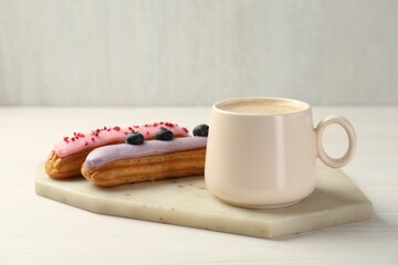 Cup of coffee and delicious eclairs covered with glaze on white wooden table