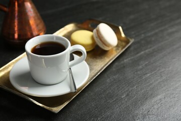 Tray with hot coffee in cup and macarons on dark textured table, closeup. Space for text